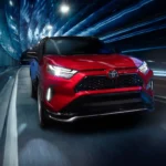 2025 Toyota RAV4 Plug-in Hybrid red front side view driving on road with tunnel and sparkling lights.